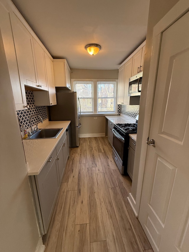 kitchen featuring sink, white cabinetry, light hardwood / wood-style flooring, appliances with stainless steel finishes, and backsplash