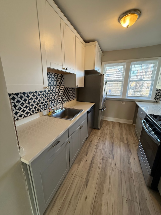 kitchen with sink, tasteful backsplash, white cabinetry, light hardwood / wood-style flooring, and appliances with stainless steel finishes