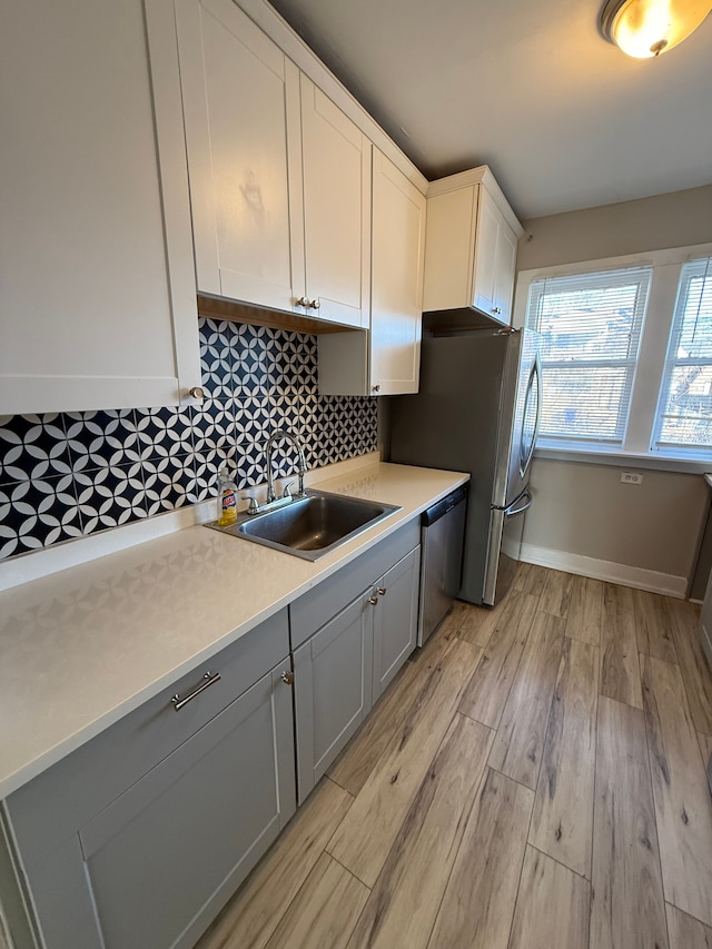 kitchen with sink, gray cabinetry, light hardwood / wood-style flooring, appliances with stainless steel finishes, and decorative backsplash