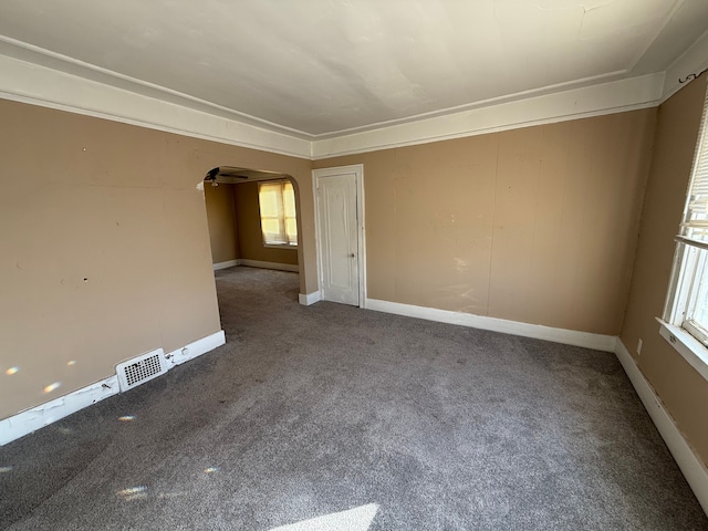 empty room featuring visible vents, arched walkways, baseboards, and carpet flooring