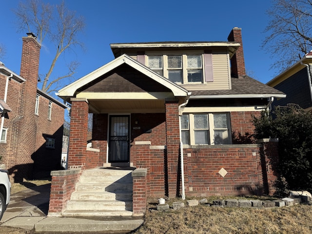 bungalow featuring brick siding, a chimney, and a shingled roof