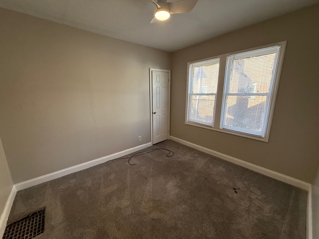 spare room with dark colored carpet, visible vents, and baseboards