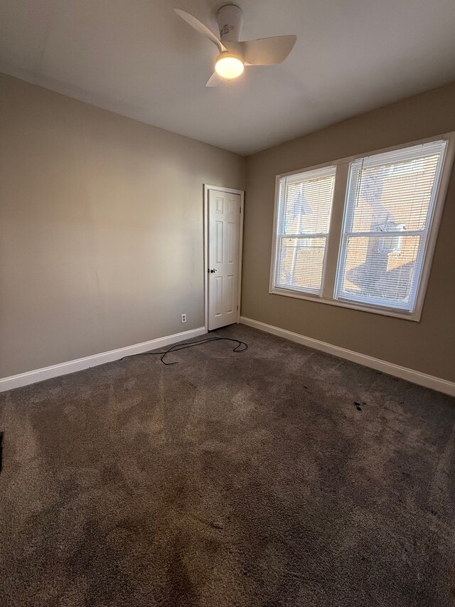 empty room with baseboards, a ceiling fan, and dark carpet