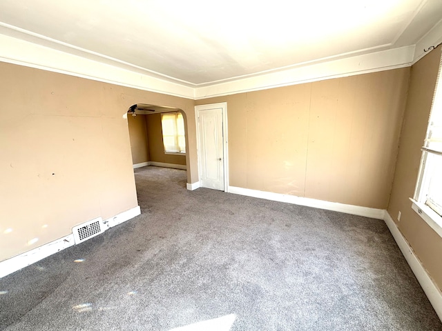 carpeted empty room featuring visible vents, arched walkways, plenty of natural light, and baseboards