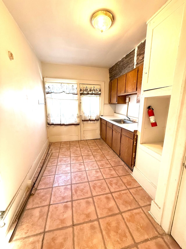 kitchen featuring light countertops, light tile patterned floors, brown cabinetry, and a sink