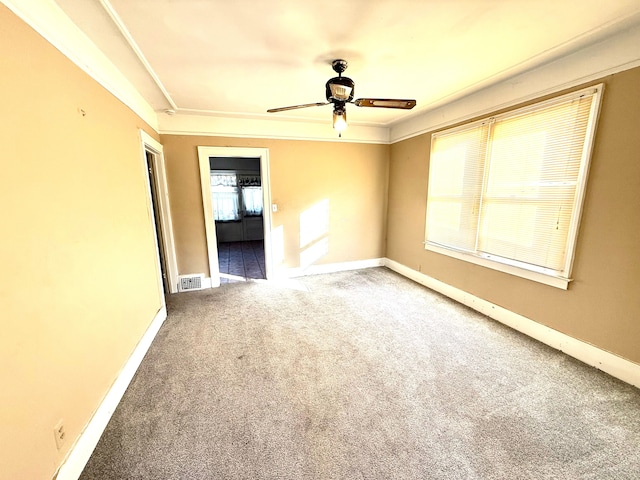 carpeted spare room featuring a ceiling fan, crown molding, baseboards, and visible vents