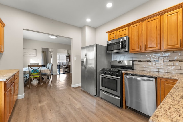 kitchen with appliances with stainless steel finishes, light stone countertops, light hardwood / wood-style floors, and decorative backsplash