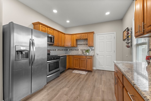 kitchen with sink, backsplash, light stone counters, stainless steel appliances, and light hardwood / wood-style flooring