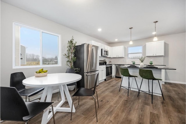 kitchen featuring appliances with stainless steel finishes, pendant lighting, white cabinets, dark hardwood / wood-style flooring, and backsplash