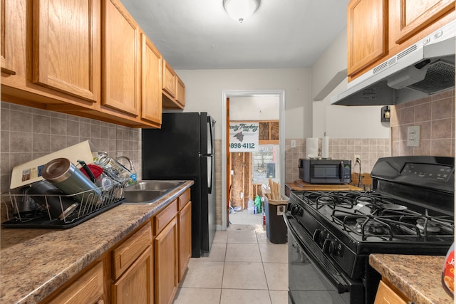 kitchen with sink, light tile patterned floors, light stone counters, and black appliances