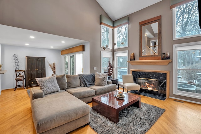 living room with a fireplace, high vaulted ceiling, and light hardwood / wood-style flooring