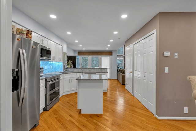 kitchen with appliances with stainless steel finishes, sink, white cabinets, a center island, and light hardwood / wood-style floors