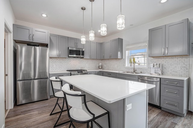 kitchen with gray cabinets, a kitchen island, sink, hanging light fixtures, and stainless steel appliances