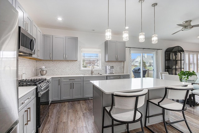 kitchen with dark wood-type flooring, decorative light fixtures, appliances with stainless steel finishes, gray cabinets, and a kitchen island