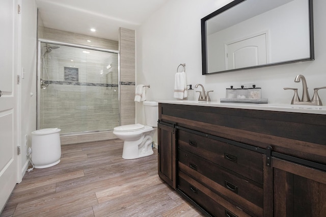 bathroom featuring a shower with door, vanity, hardwood / wood-style floors, and toilet