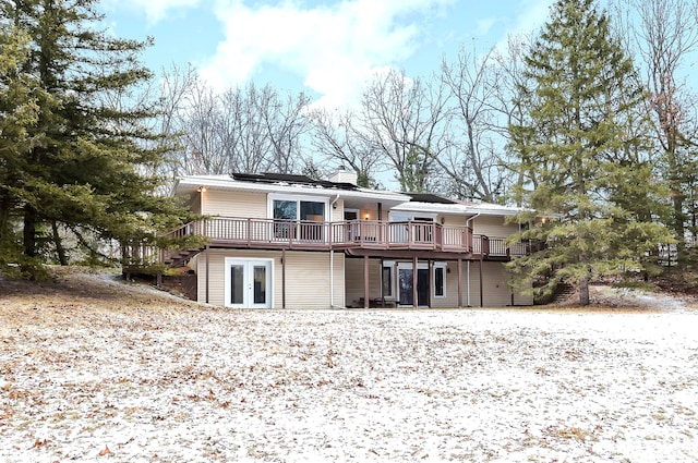 snow covered back of property featuring french doors and a wooden deck