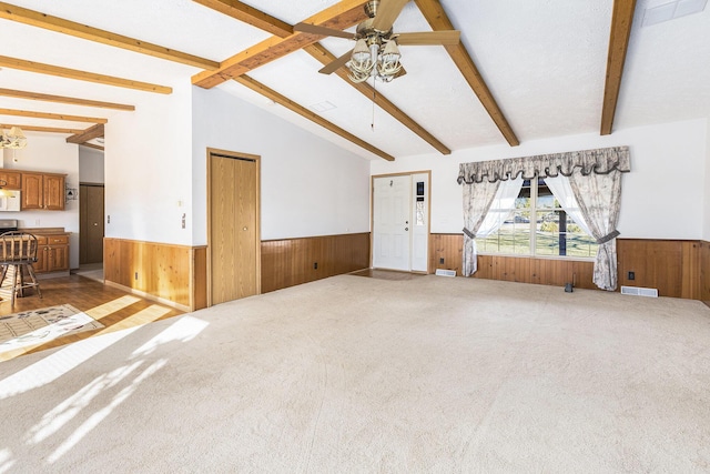 unfurnished living room featuring ceiling fan, wooden walls, and vaulted ceiling with beams