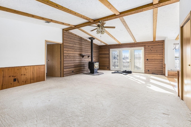 unfurnished living room featuring vaulted ceiling with beams, a textured ceiling, a wood stove, log walls, and carpet