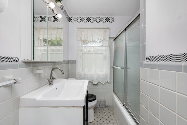 full bathroom featuring bath / shower combo with glass door, vanity, toilet, and tile walls