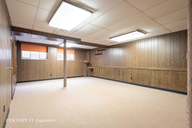 basement with light carpet, a paneled ceiling, and wooden walls