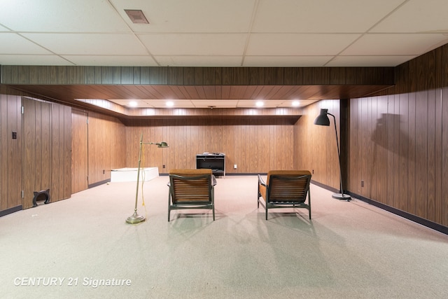 interior space featuring light colored carpet, a drop ceiling, and wood walls