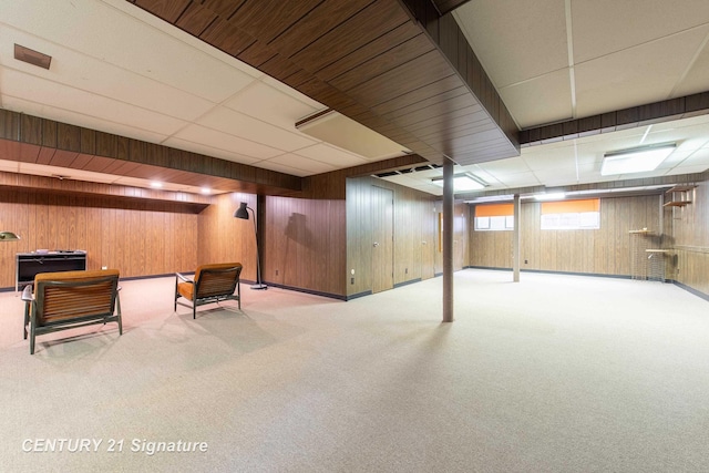 basement featuring light carpet, a drop ceiling, and wooden walls