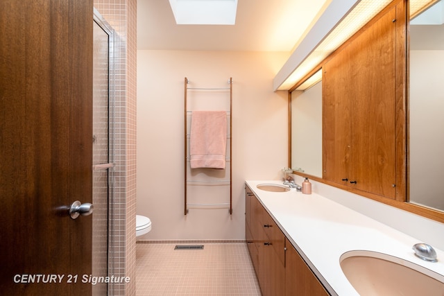 bathroom with a skylight, vanity, a shower with shower door, tile patterned floors, and toilet