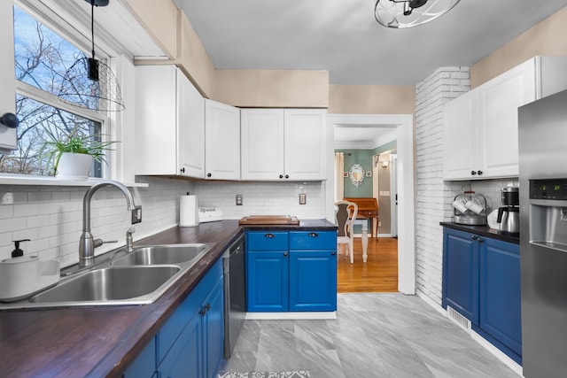 kitchen with appliances with stainless steel finishes, blue cabinets, butcher block counters, sink, and white cabinets