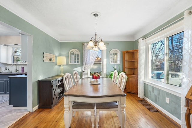 dining area with light hardwood / wood-style floors, ornamental molding, a chandelier, and sink