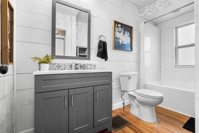 full bathroom featuring hardwood / wood-style flooring, tile walls, vanity, toilet, and tiled shower / bath