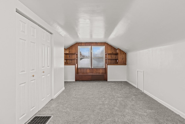 bonus room with built in shelves, light colored carpet, and lofted ceiling