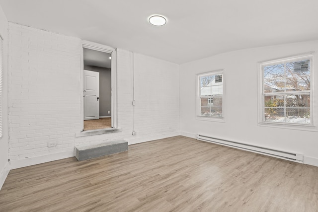 spare room with a baseboard heating unit, light hardwood / wood-style floors, and brick wall