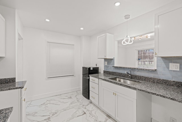 kitchen with hanging light fixtures, white cabinetry, sink, and dark stone counters