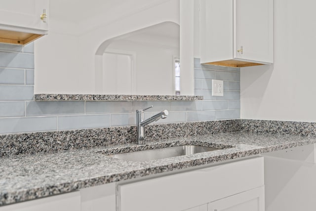 interior details featuring white cabinetry, sink, and light stone countertops