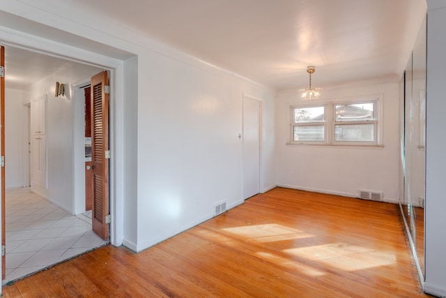 spare room featuring a notable chandelier and light wood-type flooring