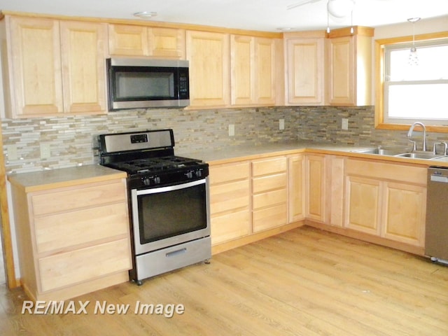 kitchen featuring light brown cabinetry, sink, hanging light fixtures, appliances with stainless steel finishes, and light hardwood / wood-style floors