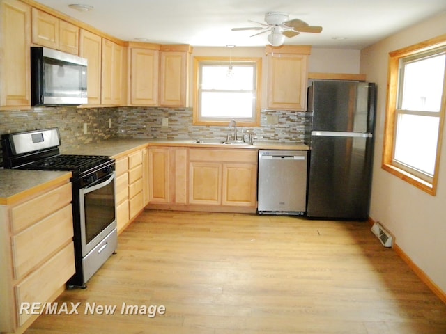 kitchen with appliances with stainless steel finishes, tasteful backsplash, sink, light brown cabinets, and light hardwood / wood-style flooring