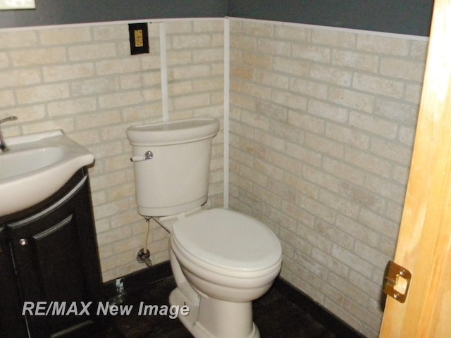 bathroom featuring vanity, brick wall, and toilet