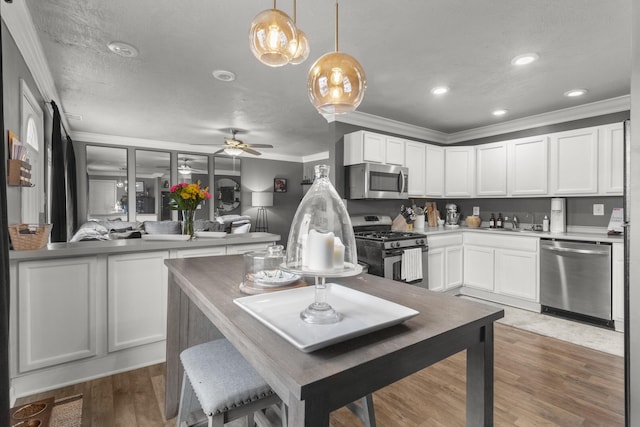 kitchen with decorative light fixtures, ornamental molding, stainless steel appliances, hardwood / wood-style floors, and white cabinets