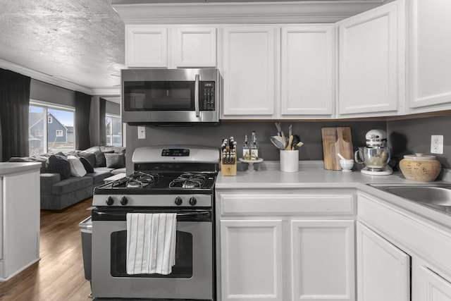 kitchen featuring stainless steel appliances, wood-type flooring, white cabinets, and a textured ceiling