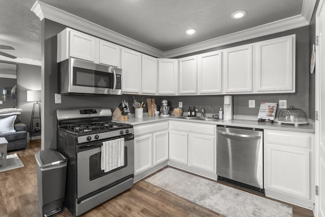 kitchen featuring sink, appliances with stainless steel finishes, ornamental molding, white cabinets, and dark hardwood / wood-style flooring