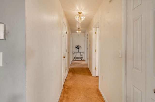 hallway featuring light colored carpet and a notable chandelier