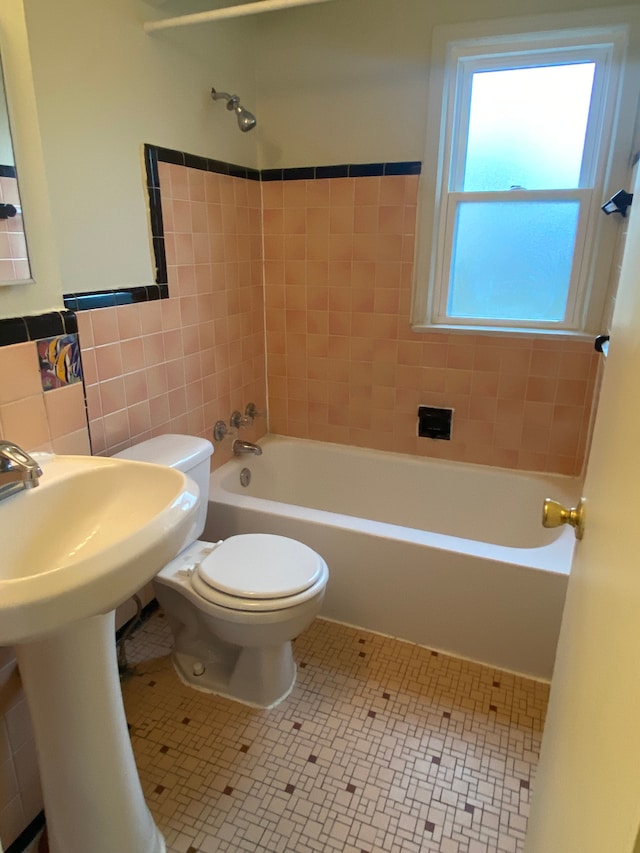 bathroom featuring tile patterned flooring, tiled shower / bath, tile walls, and toilet