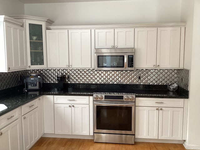 kitchen with appliances with stainless steel finishes, dark stone countertops, white cabinets, and backsplash