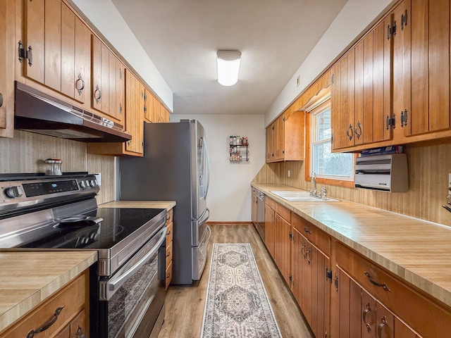 kitchen with appliances with stainless steel finishes, sink, backsplash, and light hardwood / wood-style flooring