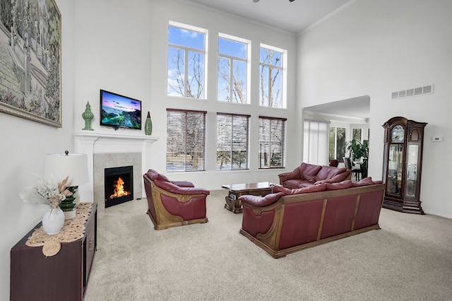 carpeted living room with a fireplace, ornamental molding, and a towering ceiling