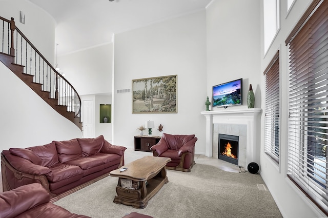 carpeted living room featuring a tiled fireplace, ornamental molding, and a towering ceiling