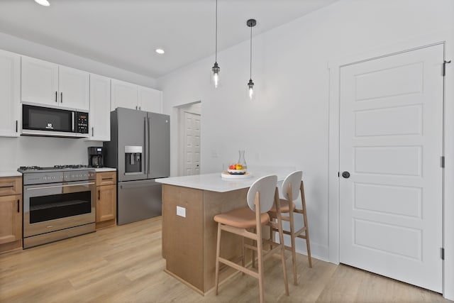 kitchen with decorative light fixtures, white cabinets, a kitchen bar, stainless steel appliances, and light hardwood / wood-style flooring