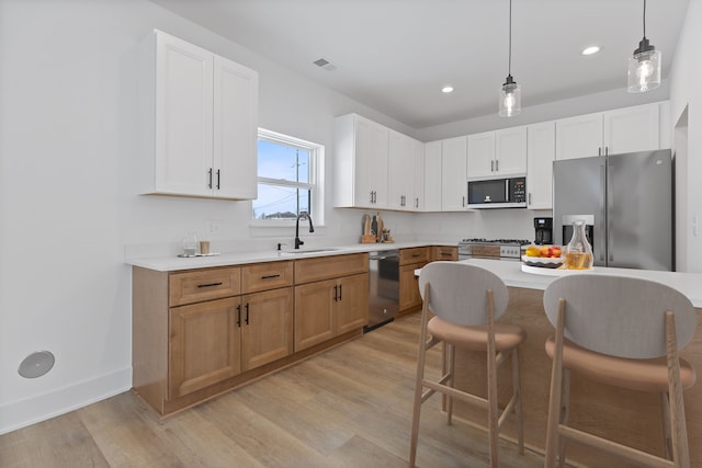 kitchen with decorative light fixtures, sink, white cabinets, stainless steel appliances, and light wood-type flooring