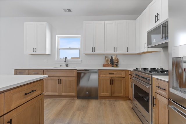 kitchen with light wood-type flooring, appliances with stainless steel finishes, sink, and white cabinets